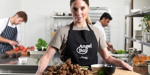 Woman wearing Angel Bay apron serving skewers with Angel Bay meatballs on.