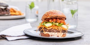 Burger with Angel Bay patty, melted cheese, and cucumber ribbons on a plate.