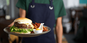 Woman in apron serving up Angel Bay burger.