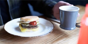 Angel Bay breakfast sausage patty in muffin split on plate next to cup of coffee.